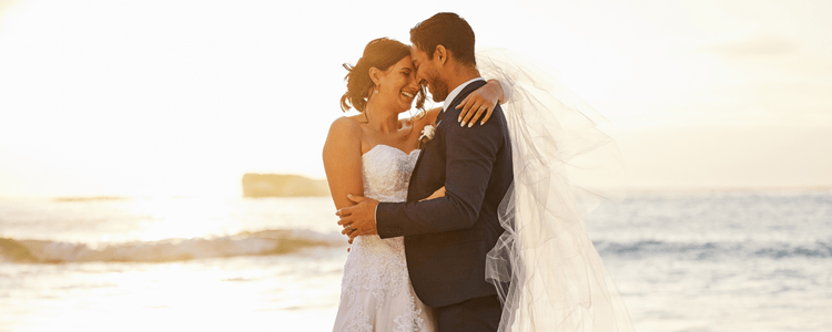 A bride and groom smile at each other on beach